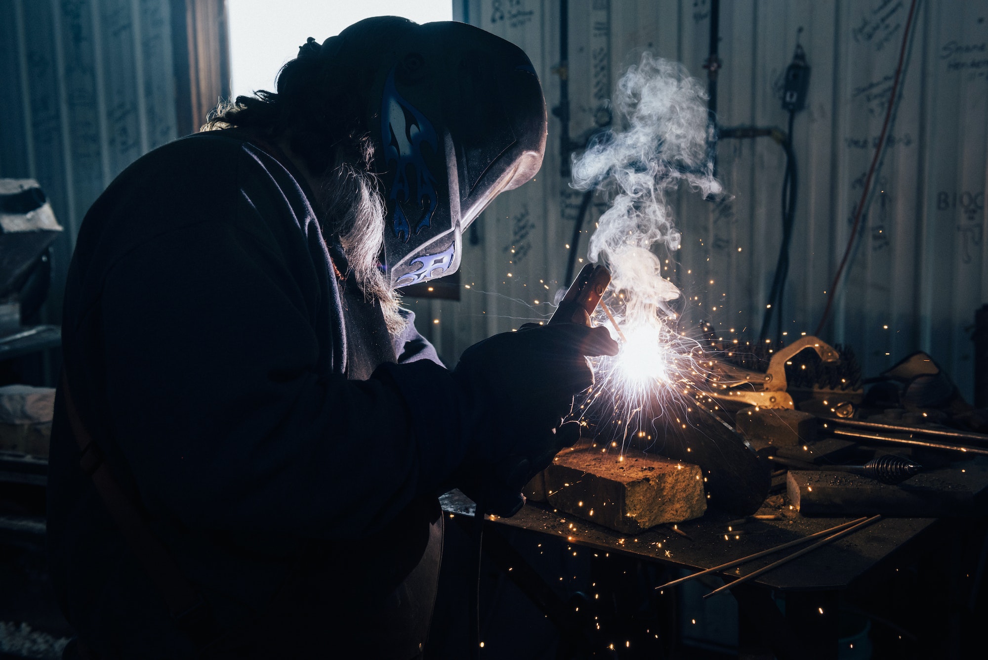 Blacksmith in welding mask welding metal in workshop