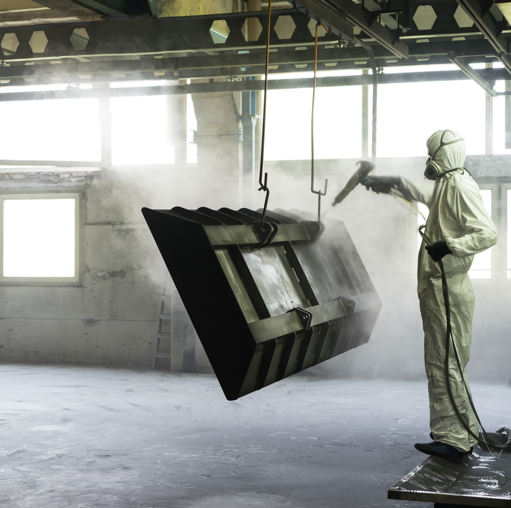 worker sand blasting a metal crate