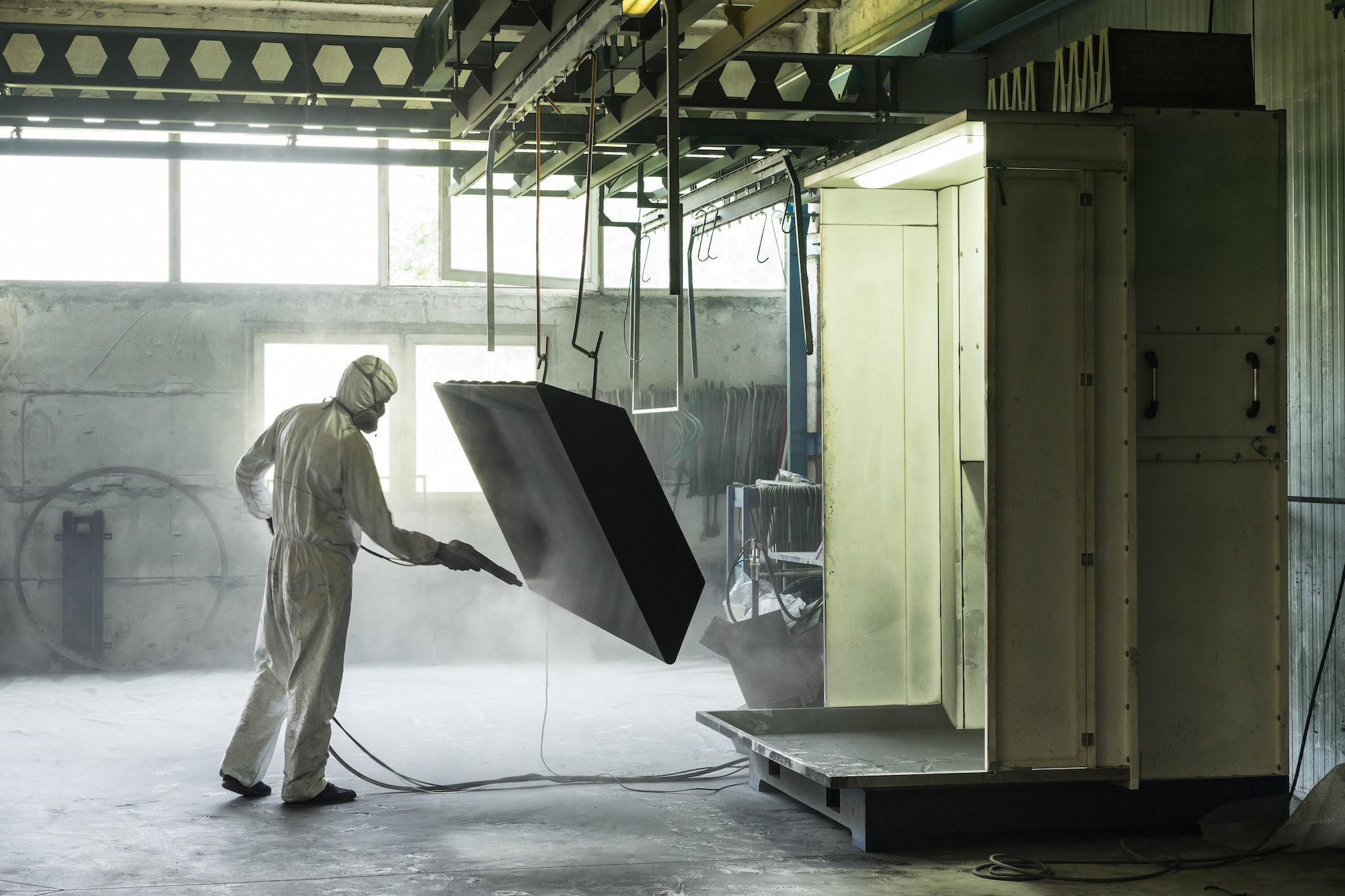 worker sand blasting a metal crate